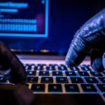 Close-up of gloved hands typing on a laptop keyboard in a dark setting