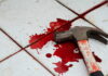 A bloody hammer resting on a tiled floor with red stains