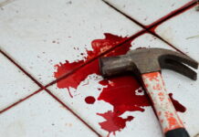 A bloody hammer resting on a tiled floor with red stains