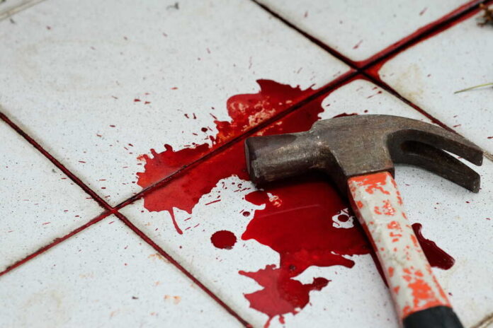 A bloody hammer resting on a tiled floor with red stains