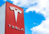 Tesla Scandal: Misleading Self-Driving Claims Exposed Tesla logo on a red corporate sign against a blue sky with clouds