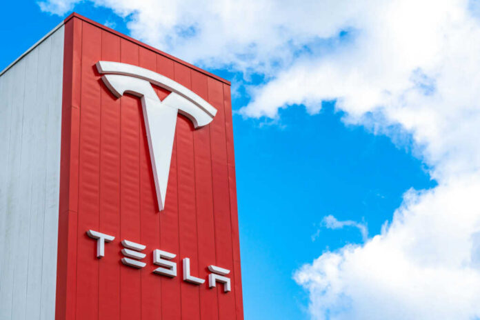 shutterstock2441514279jpg Tesla logo on a red corporate sign against a blue sky with clouds