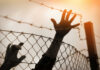 Silhouette of a hand reaching through a barbed wire fence
