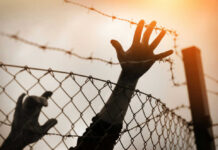 Silhouette of a hand reaching through a barbed wire fence