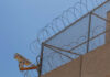 Security camera mounted on a barbed wire fence against a clear blue sky
