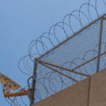 Security camera mounted on a barbed wire fence against a clear blue sky