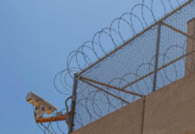 Security camera mounted on a barbed wire fence against a clear blue sky