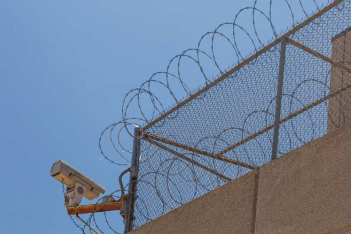 Security camera mounted on a barbed wire fence against a clear blue sky