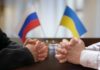 Clasped hands of two individuals with Russian and Ukrainian flags in the background