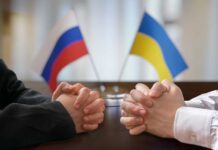 Clasped hands of two individuals with Russian and Ukrainian flags in the background