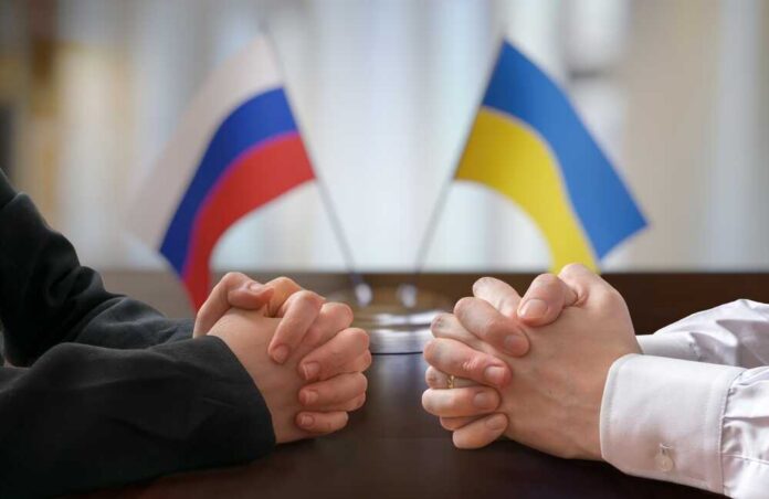 Clasped hands of two individuals with Russian and Ukrainian flags in the background