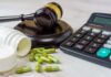 A gavel, medication capsules, and a calculator on a table