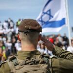 Soldier saluting in front of a crowd with the Israeli flag in the background