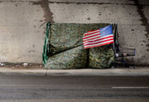 A makeshift shelter draped with an American flag next to a shopping cart on a city street