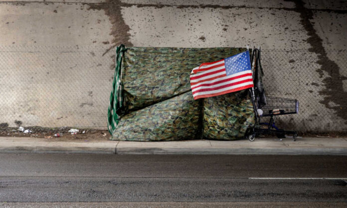 A makeshift shelter draped with an American flag next to a shopping cart on a city street