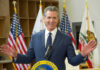 Newsom’s Gas Blame Game Targets Trump California governor speaking at a podium with flags in the background