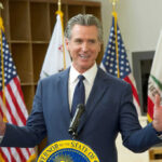 California governor speaking at a podium with flags in the background