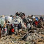 Displaced families with belongings crowd a rubble-strewn road