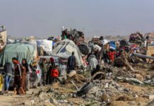 Displaced families with belongings crowd a rubble-strewn road