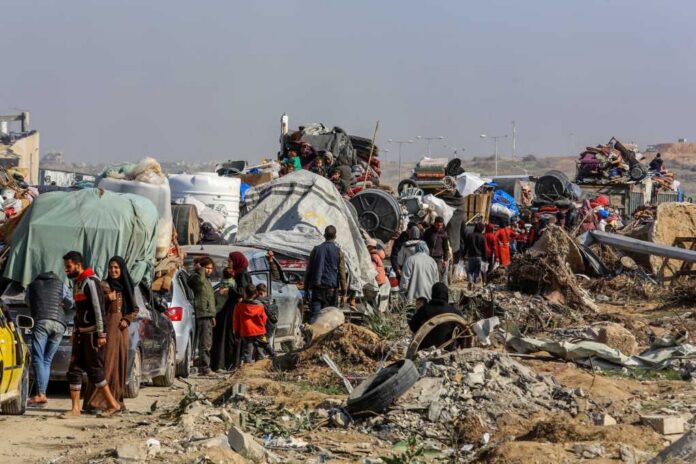 Displaced families with belongings crowd a rubble-strewn road