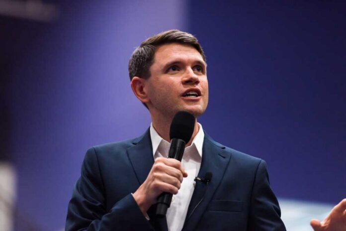 A man in a suit speaking into a microphone at a conference