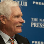 A man with gray hair and a mustache smiling during a press conference