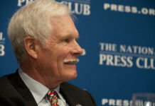 A man with gray hair and a mustache smiling during a press conference