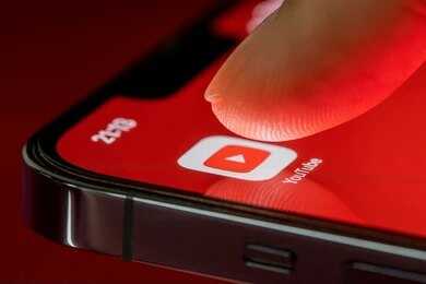 Finger tapping YouTube app icon on smartphone screen