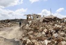 Southern Lebanon Pays The Price Again Person walking past rubble and destroyed buildings on a dirt road