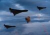Three military drones fly through a cloudy sky amid anti-air fire