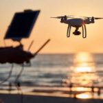 A drone flying over a beach at sunset with a person controlling it