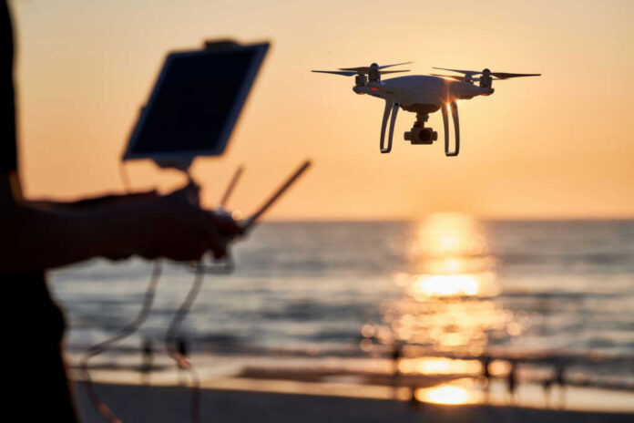 A drone flying over a beach at sunset with a person controlling it