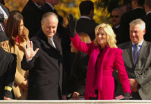 Two public figures waving at an outdoor event surrounded by a crowd