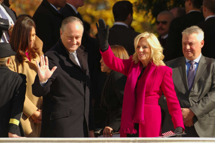 Two public figures waving at an outdoor event surrounded by a crowd