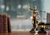 A bronze statue of Lady Justice holding scales and a sword, with law books and a gavel in the foreground