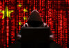 America’s AI Secrets Under Attack A hooded figure sitting in front of a laptop with a red digital background