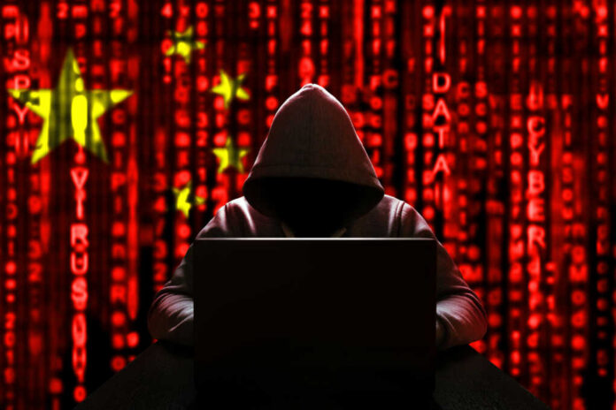 shutterstock_1652741782 A hooded figure sitting in front of a laptop with a red digital background