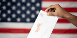 A hand placing a ballot into a voting box with an American flag background