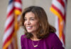 Health Perk for Prostitutes — Why? Smiling woman in a purple outfit with American flags in the background