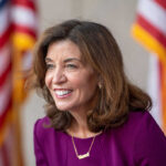 Health Perk for Prostitutes — Why? Smiling woman in a purple outfit with American flags in the background
