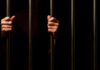 Second Death, Same ICE Jail — Why? Hands gripping prison bars against a dark background
