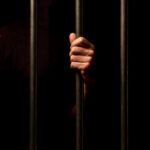 Hands gripping prison bars against a dark background