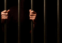 Second Death, Same ICE Jail — Why? Hands gripping prison bars against a dark background
