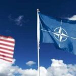 Flags of various nations displayed outside NATO headquarters under a clear blue sky