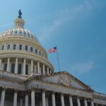 Ally at “Critical” — Capitol Charges Ahead The U.S. Capitol building with an American flag flying against a blue sky