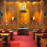 Judge TORCHES DOJ: ‘Blatantly Unlawful’ Interior view of a courtroom with wooden paneling and red seating