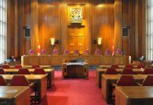 Judge TORCHES DOJ: ‘Blatantly Unlawful’ Interior view of a courtroom with wooden paneling and red seating