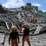Person walking past rubble and destroyed buildings on a dirt road