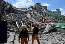 Person walking past rubble and destroyed buildings on a dirt road