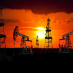Silhouetted oil rigs against a vibrant sunset